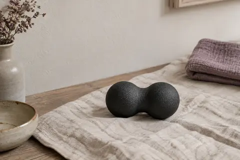 Balle de massage double noire en EPP posée sur un tapis de lin dans un intérieur calme