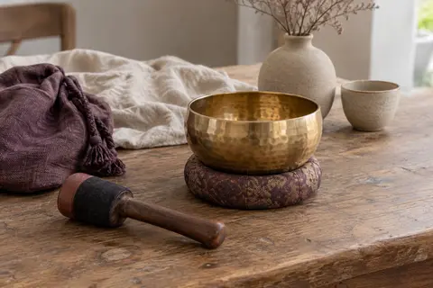 Bol chantant tibétain martelé doré avec maillet double face, coussin en anneau et sac sur une table en bois.
