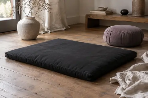 Tapis zabuton noir en coton posé au sol près d’un coussin de méditation dans un intérieur calme