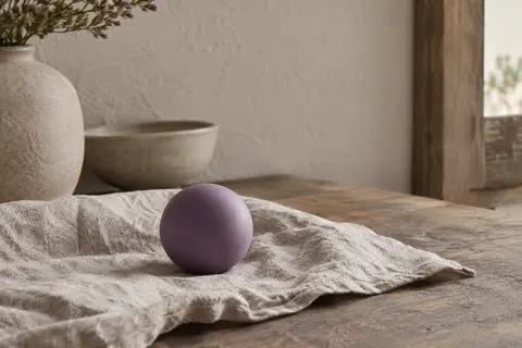 Balle de massage violette en silicone posée sur du lin dans un intérieur calme et lumineux
