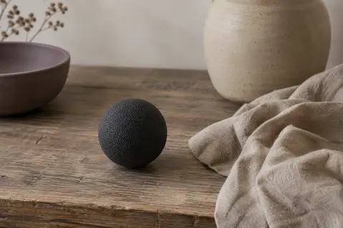 Balle de massage Blackroll noire en mousse posée sur du lin froissé dans un intérieur calme.