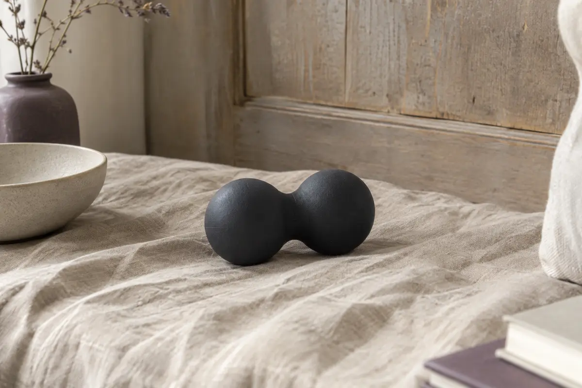 Double balle de massage noire posée sur un tissu de lin froissé dans un intérieur calme.