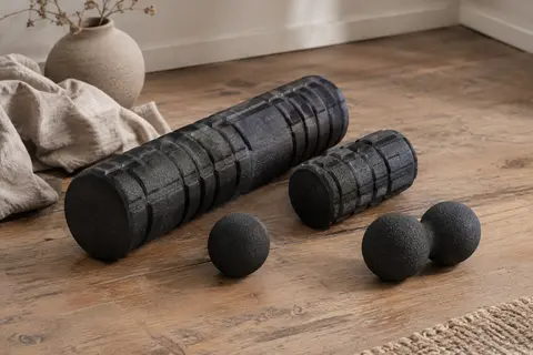 Kit noir avec rouleaux de massage standard et mini, balle et double-balle posés sur un sol en bois