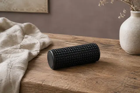 Petit rouleau d’automassage noir à relief structuré posé sur une table en bois près d’un tissu de lin