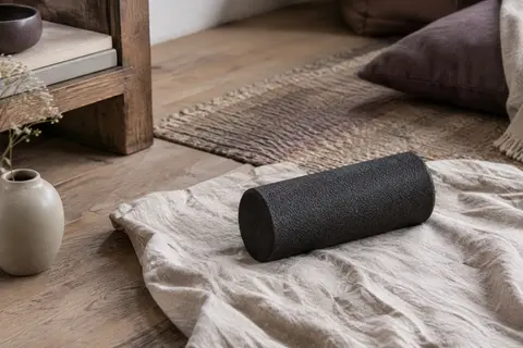 Petit rouleau d’automassage noir en mousse posé sur un linge de lin dans un intérieur calme.