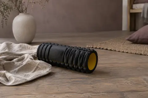 Rouleau cylindrique de massage noir et jaune posé sur du lin dans un intérieur calme.