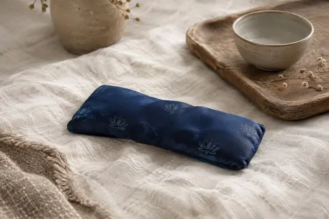 Coussinet pour les yeux en soie bleu foncé à motif lotus posé sur du lin ivoire froissé