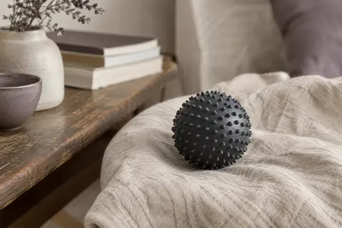 Balle de massage anthracite à picots posée sur un linge de lin dans un intérieur calme et lumineux.