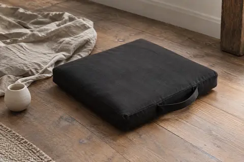 Zabuton carré noir en coton posé sur un parquet, avec sa sangle de transport assortie visible