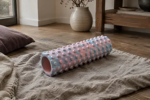 Rouleau de massage en mousse à relief 3D rose et bleu posé sur un tapis dans un intérieur calme.