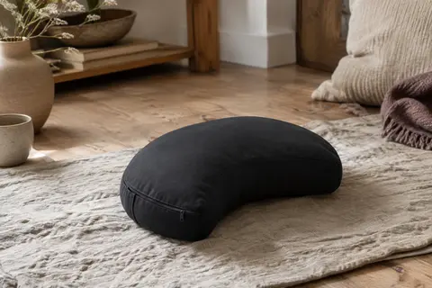Coussin de méditation noir en forme de demi-lune posé sur un tapis de lin dans un intérieur calme.