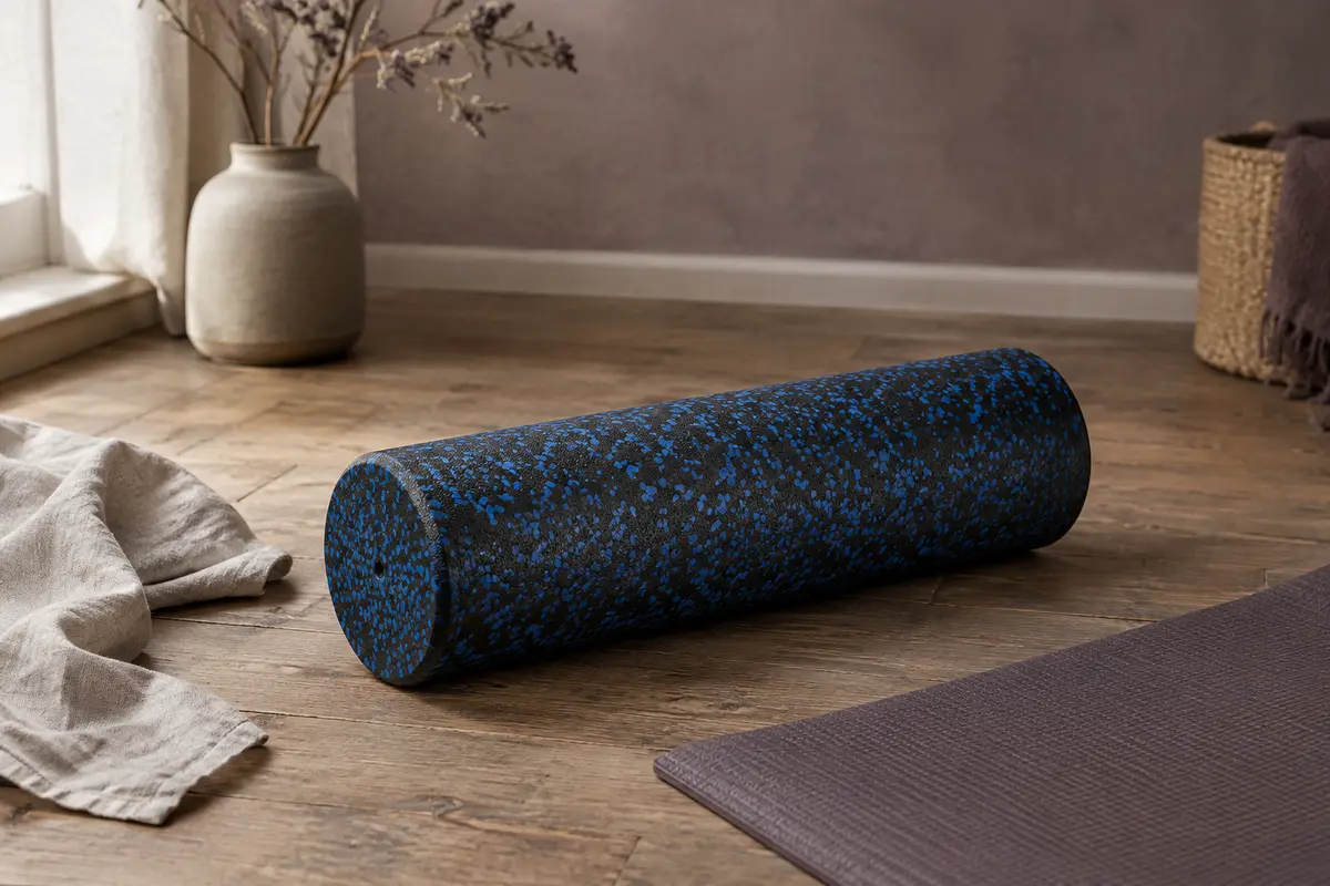 Rouleau de massage lisse noir et bleu posé sur un tapis, dans un intérieur calme aux matières naturelles.