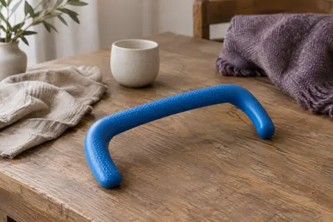 Canne de massage incurvée en polyéthylène bleu posée sur une table en bois dans un intérieur calme