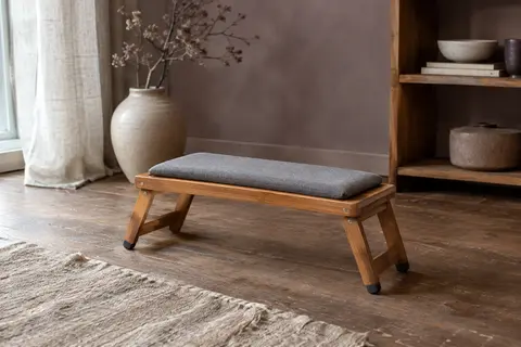 Banc de méditation pliable en bambou brun avec coussin gris, posé sur un sol en bois