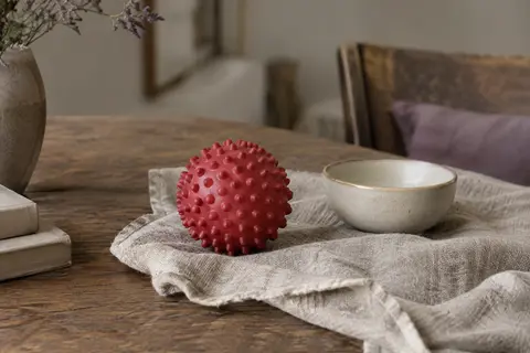 Balle de massage rouge à reliefs bosselés posée sur un linge de lin dans un intérieur calme