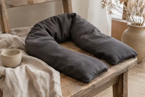 Bouillotte cervicale en tissu gris anthracite posée sur du lin froissé dans un intérieur calme