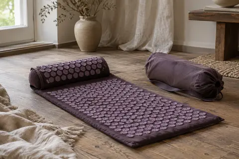 Tapis d’acupression pourpre partiellement déroulé près de son sac de transport dans un intérieur calme.
