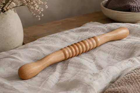 Rouleau de massage corporel courbé en bois posé sur du lin dans un intérieur calme.