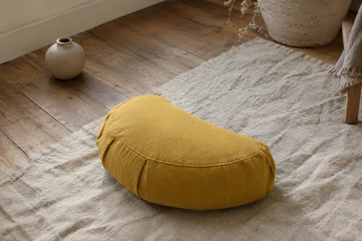 Coussin de méditation demi-lune en coton jaune indien posé sur un tapis de lin dans un intérieur calme