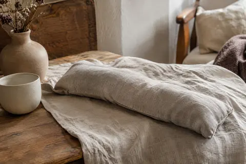 Bouillotte sèche longue en coton posée sur du lin froissé dans un intérieur calme
