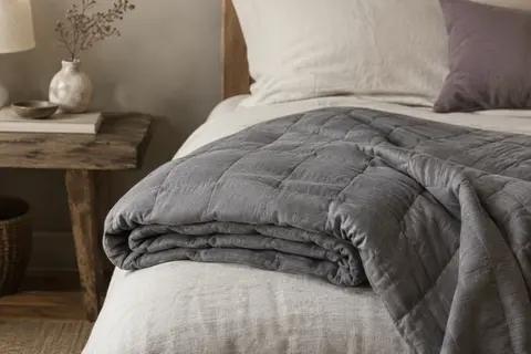 Couverture lestée grise en coton, pliée sur un lit dans une chambre à la lumière douce.