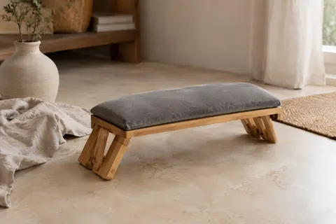 Banc de méditation pliable en bambou avec coussin gris en velours, posé dans un intérieur calme.