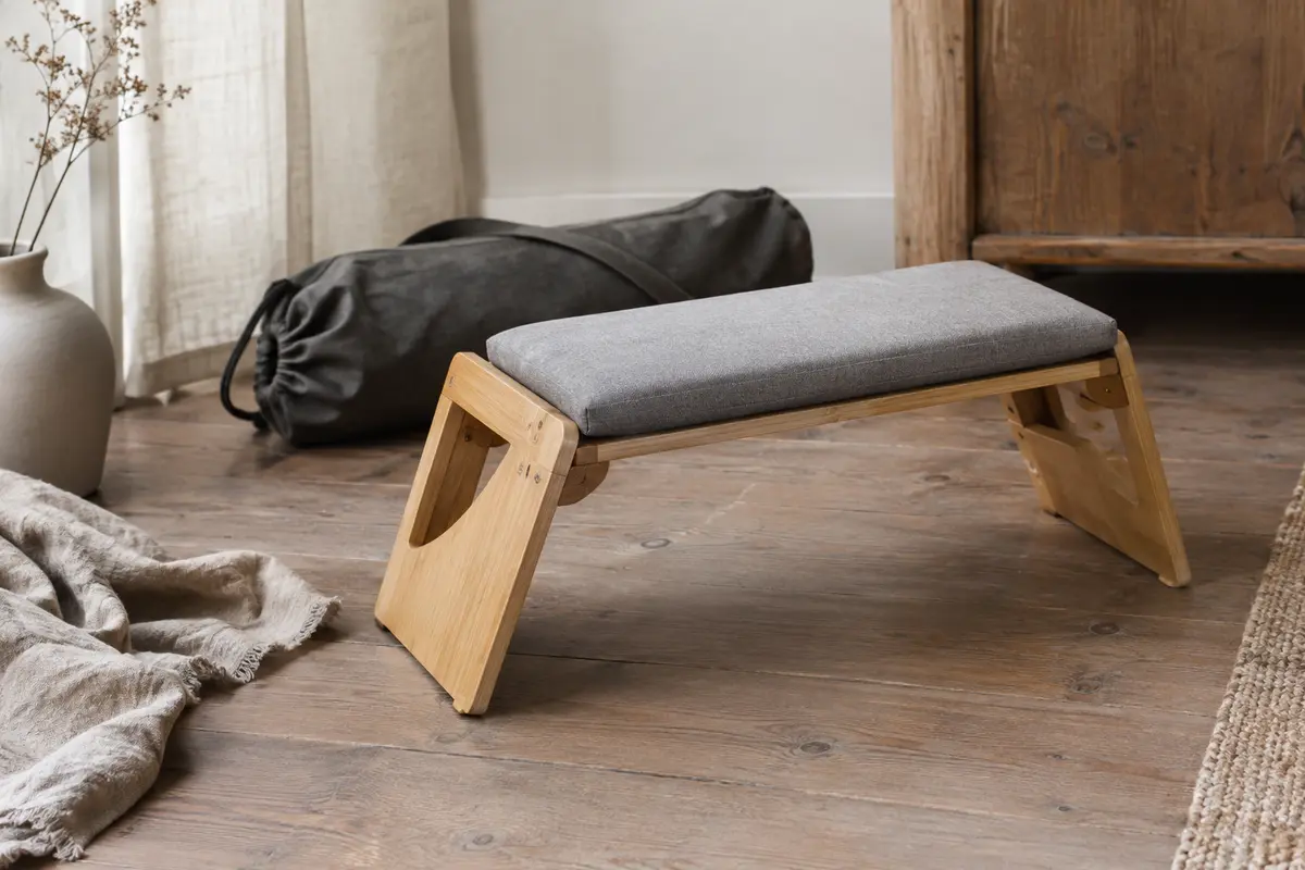 Banc de méditation pliable en bambou avec coussin gris amovible et sac de transport, posé dans un intérieur calme.