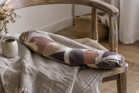 Coussin Cervico multicolore aux noyaux de cerise posé en courbe sur un fauteuil en bois
