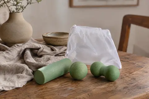 Kit vert de massage avec mini rouleau, balle simple et balle double disposés sur un linge clair