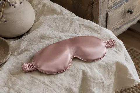 Masque de nuit rose en soie de mûrier, coques profilées 3D et sangle réglable posés sur du lin.