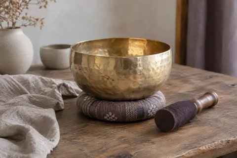 Bol chantant doré martelé posé sur un coussin, avec son maillet en bois et cuir à côté