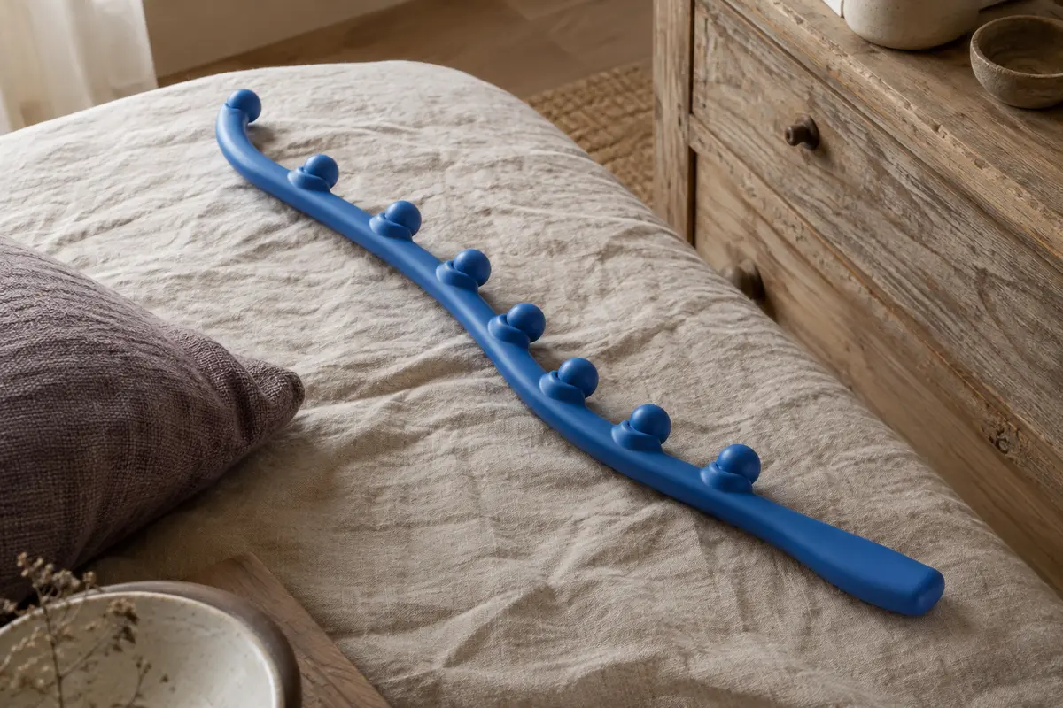 Canne de massage bleue à huit nœuds posée sur du lin près d’un meuble en bois.