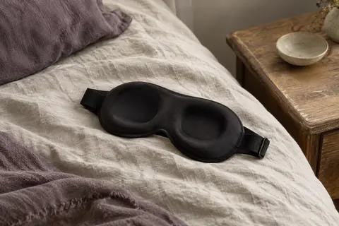 Masque de nuit noir à contour 3D posé sur du lin froissé dans un intérieur calme