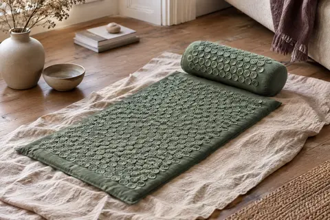 Tapis d’acupression vert et coussin assorti posés sur du lin froissé dans un intérieur calme.