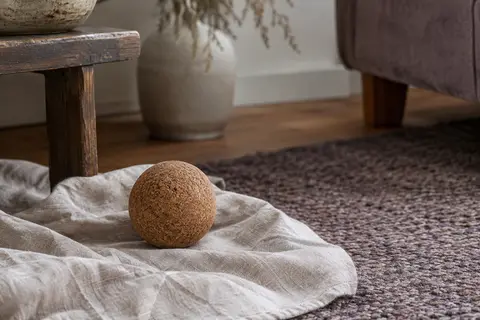 Balle ronde de massage en liège brun posée sur un linge de lin dans un intérieur calme.