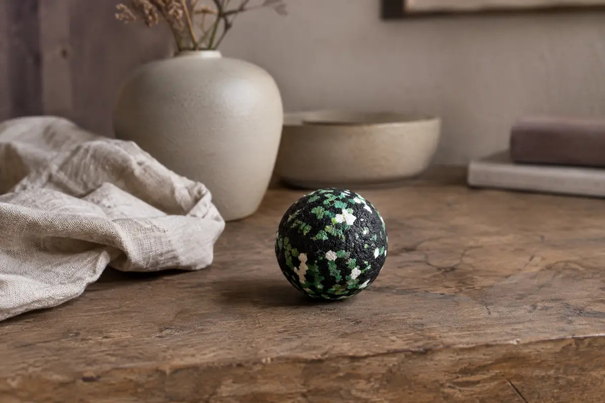 Balle de massage compacte en mousse verte, noire et blanche posée sur du bois avec du lin froissé