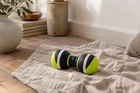 Rouleau de massage à double balle réglable posé sur un tapis de lin dans un intérieur calme
