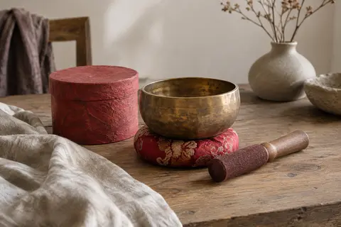 Bol chantant cuivré posé sur un coussin rouge brodé, avec maillet en bois et boîte artisanale Lokta.