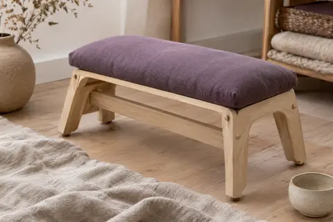Banc de méditation pliant en bouleau avec assise rembourrée violette, posé dans un intérieur calme.