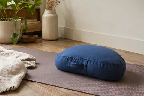 Coussin de méditation demi-lune bleu en coton avec poignée, posé sur un tapis dans un intérieur calme.