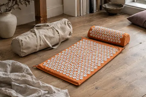 Tapis d’acupression Wellax orange avec coussin assorti et sac de transport dans un intérieur calme.
