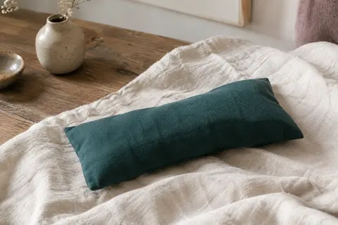Coussin pour les yeux en coton vert océan posé sur du lin froissé dans un intérieur calme