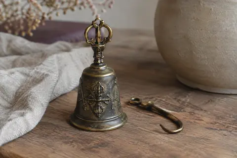 Clochette tibétaine en laiton patiné avec Dorje Vajra en relief, posée sur du bois près d’un tissu de lin